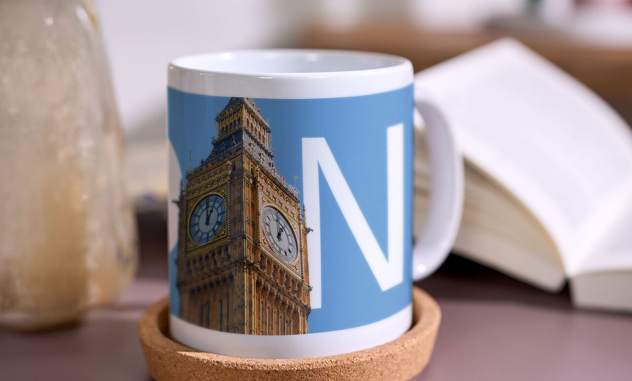Fototasse mit Stadtmotiv zeigt den Uhrturm Big Ben und den Buchstaben N, steht auf einem Untersetzer neben einem Buch