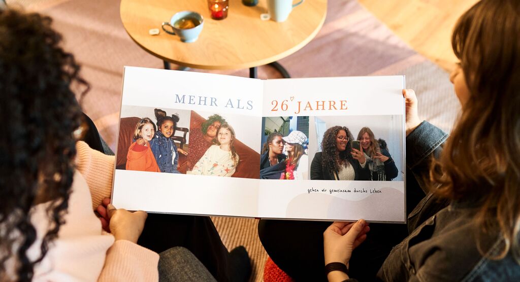 Zwei Menschen zeigen ein Fotobuch mit Erinnerungen zu 26 Jahren.