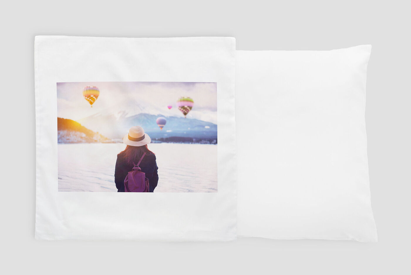 Eine Frau mit Sonnenhut und Rucksack blickt auf eine Landschaft mit bunten Heißluftballons am Himmel