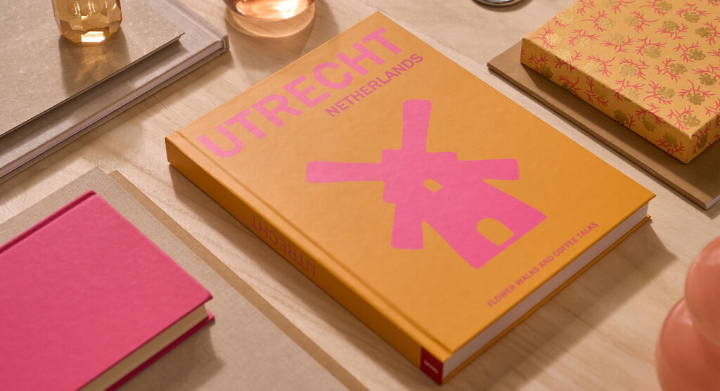 Auf einem Tisch liegt ein CEWE FOTOBUCH. Das Cover ist orange und mit dem Schriftzug „Utrecht“ gestaltet.
