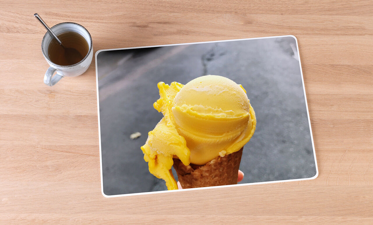 Ein köstliches gelbes Eis auf einer Waffel, gehalten in einer Hand, mit einem Kaffee daneben