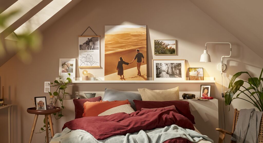 Ein gemütliches Schlafzimmer mit einem großen Wandbild von einem Paar in der Wüste, umgeben von persönlichen Fotos und Pflanzen
