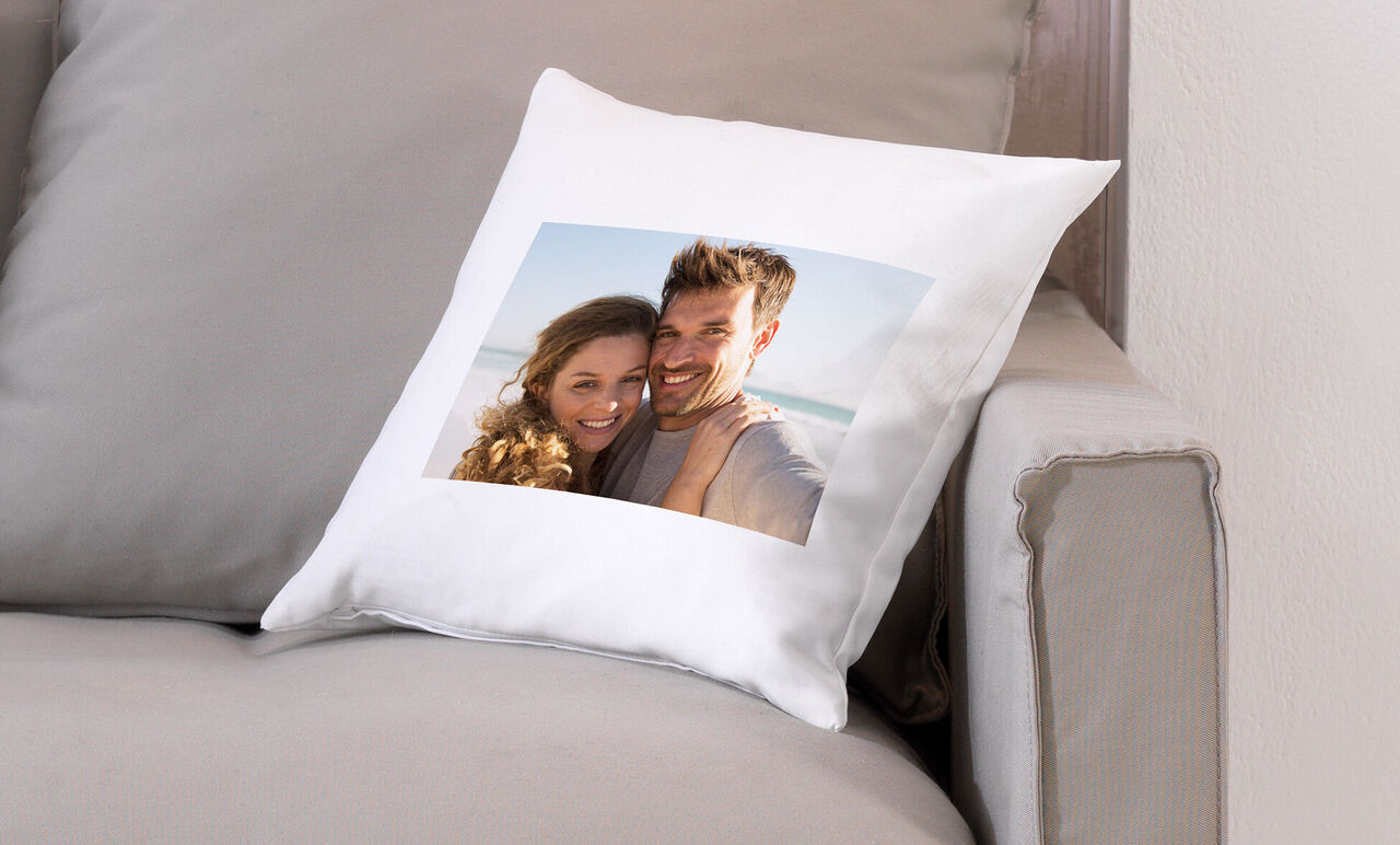 Kissen mit einem Foto von zwei Personen am Strand, strahlender Sonnenschein auf einer gemütlichen Couch.