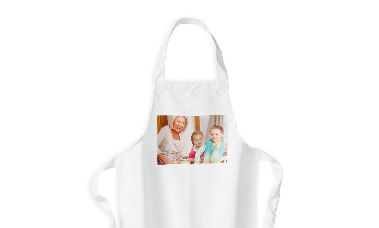 Eine weiße Schürze mit einem fröhlichen Familienfoto von einer älteren Frau und zwei Kindern, die zusammen Spaß beim Backen haben