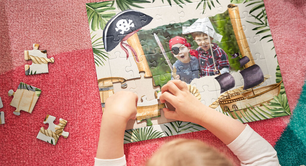 Ein Kind setzt ein Puzzle mit Piratenthema zusammen. Szenen aus einem Abenteuer sind sichtbar.