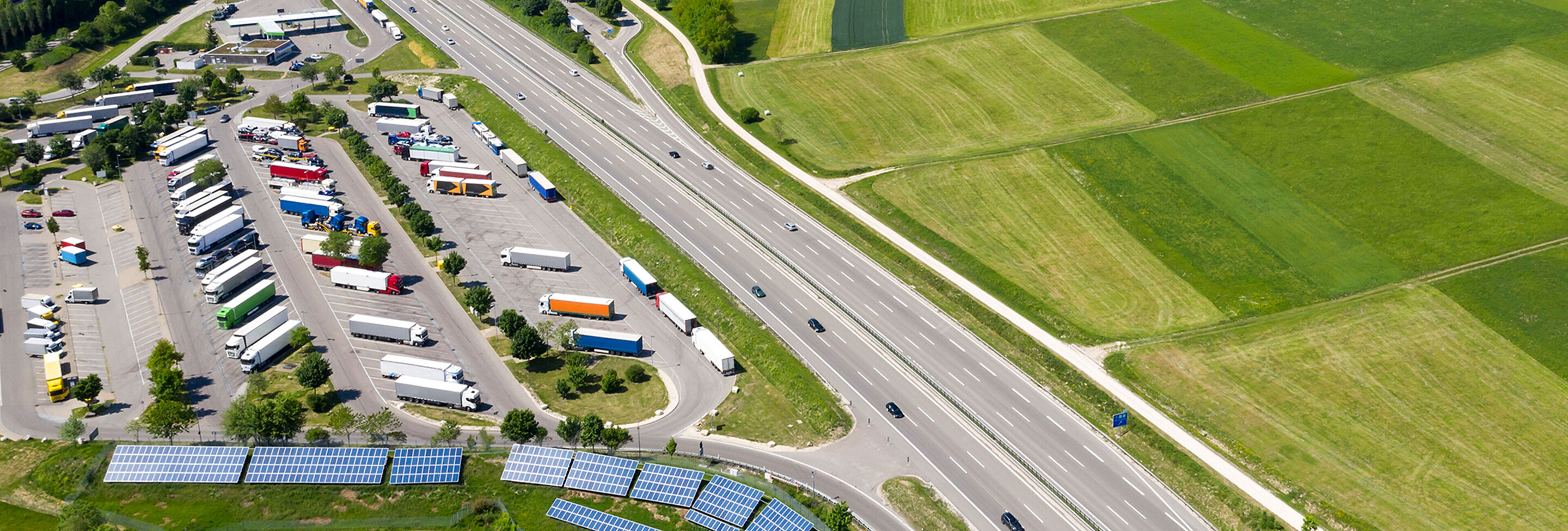 Luftaufnahme von einer Autobahn mit angrenzendem Parkplatz für Lkw und Solarpanelen