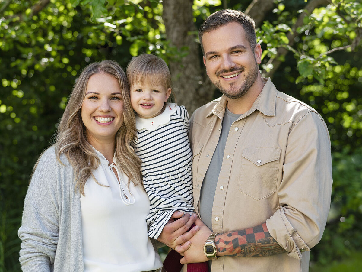 Eine liebevolle Familie steht im Freien, umgeben von grünem Laub. Sie strahlen Freude und Zusammengehörigkeit aus.