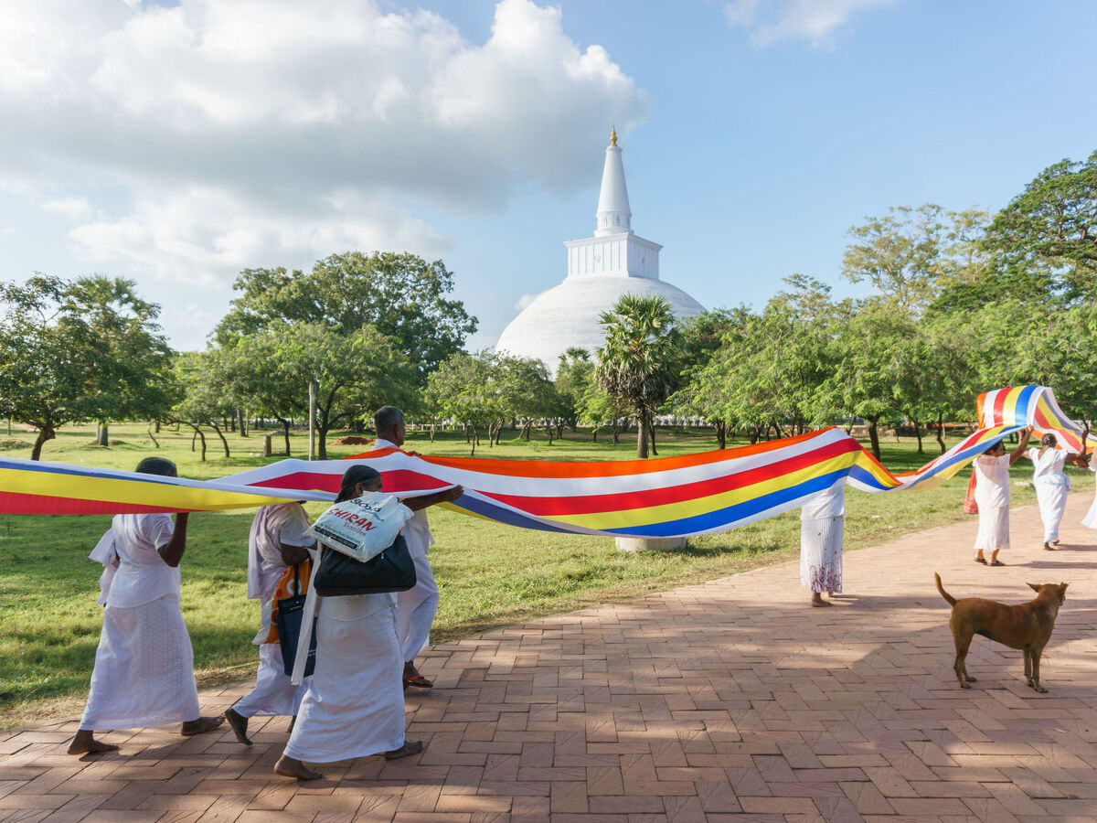 Gläubige tragen eine große bunte Fahne vor einer Pagode im Freien