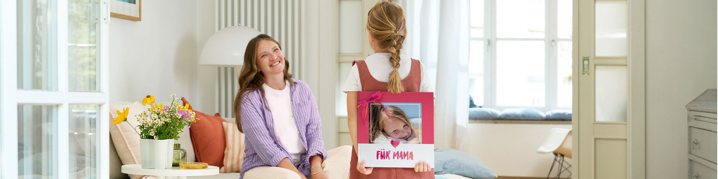 Ein Kind überrascht eine Frau mit einem Fotobuch auf einem Tisch.