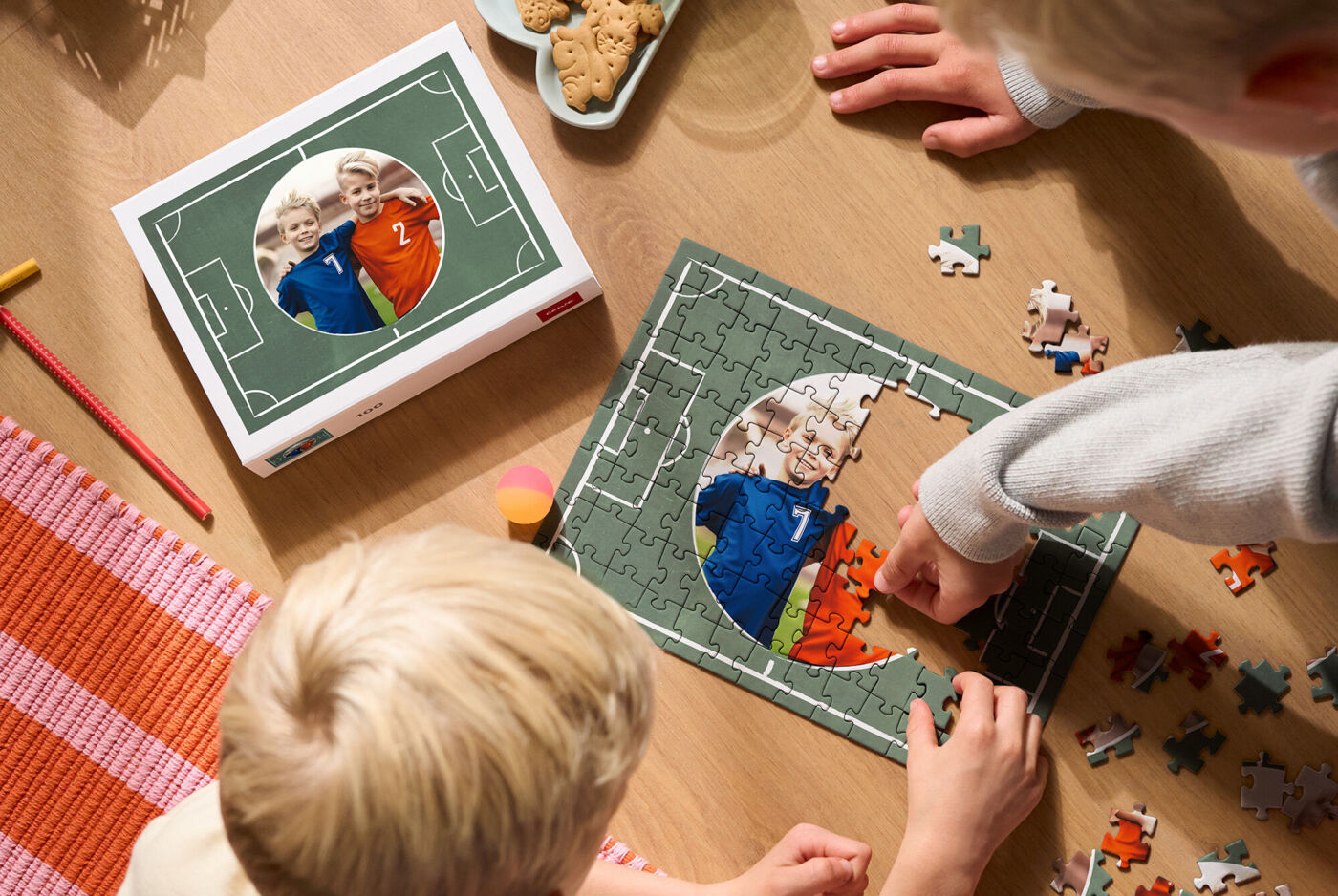 Hände legen Foto-Puzzle auf Holztisch, Puzzlebox im Hintergrund.