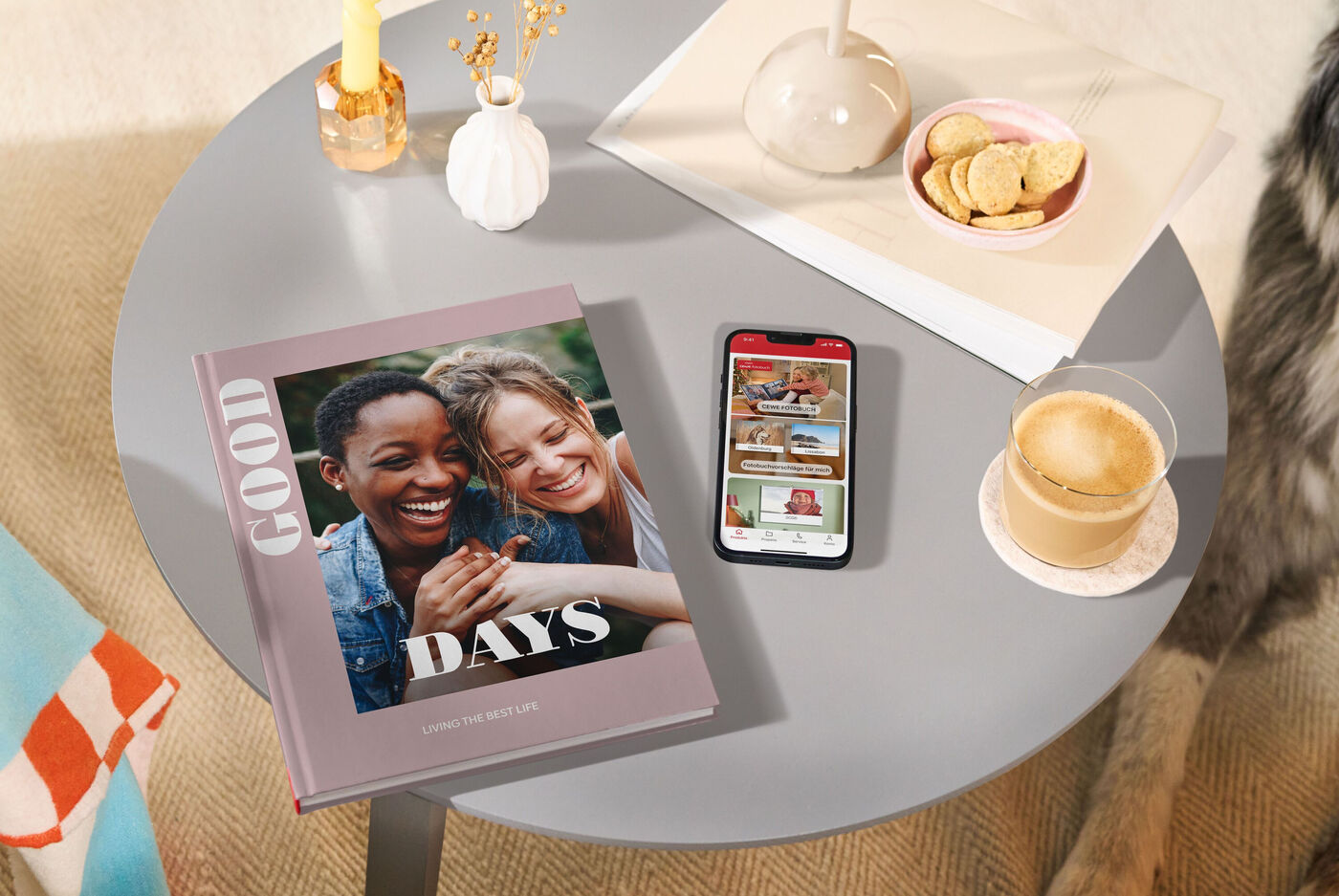 CEWE FOTOBUCH und Smartphone mit CEWE App auf rundem Couchtisch.