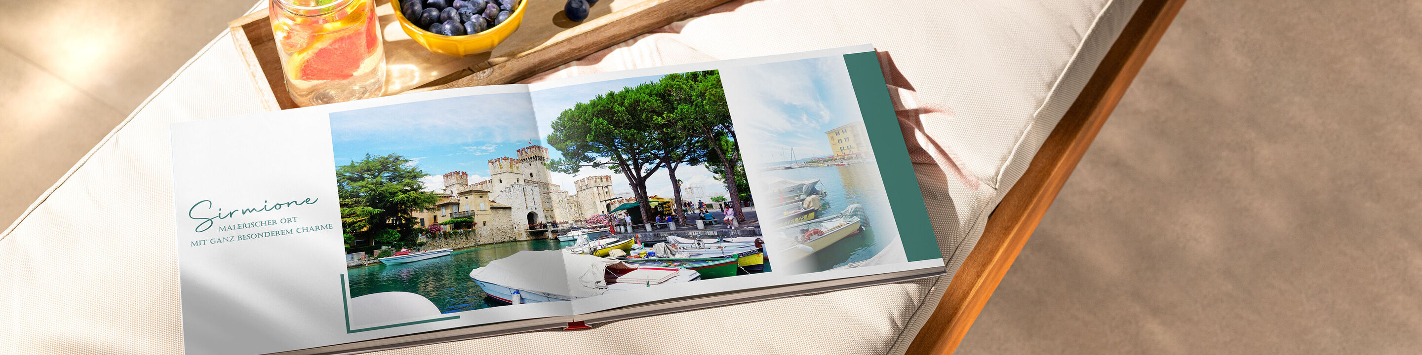 Ein geöffnetes CEWE Fotobuch auf einer Liege mit einem schönen Urlaubsmotiv. Daneben steht eine Schale mit Blaubeeren.