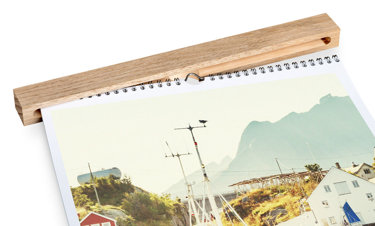 Ein CEWE Fotokalender zeigt eine malerische Küstenlandschaft mit Bergen, die im Hintergrund sichtbar sind.