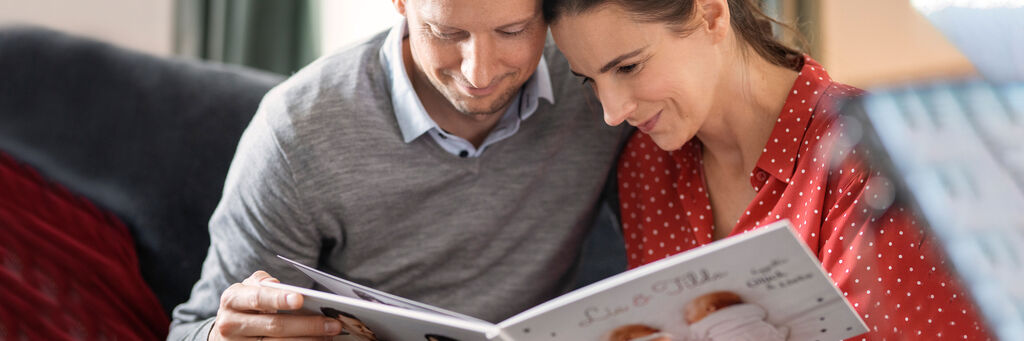 Ein Paar gemeinsam in einem gemütlichen Raum, das durch ein Fotobuch blättert und Freude teilt