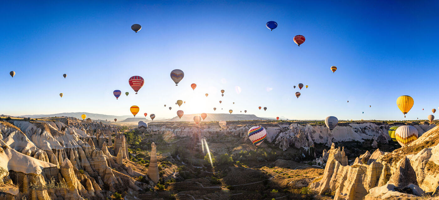 Bunte Heißluftballons schweben über einer beeindruckenden Landschaft mit Felsen und Tälern unter einem klaren, blauen Himmel