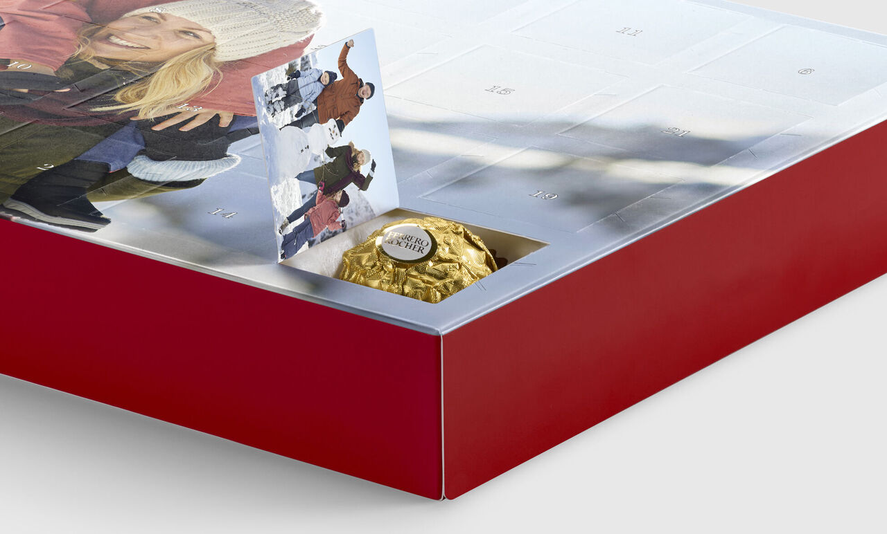 Ein roter Adventskalender mit einem goldenen Schokoladenkügelchen und einem kleinen Weihnachtsbild.