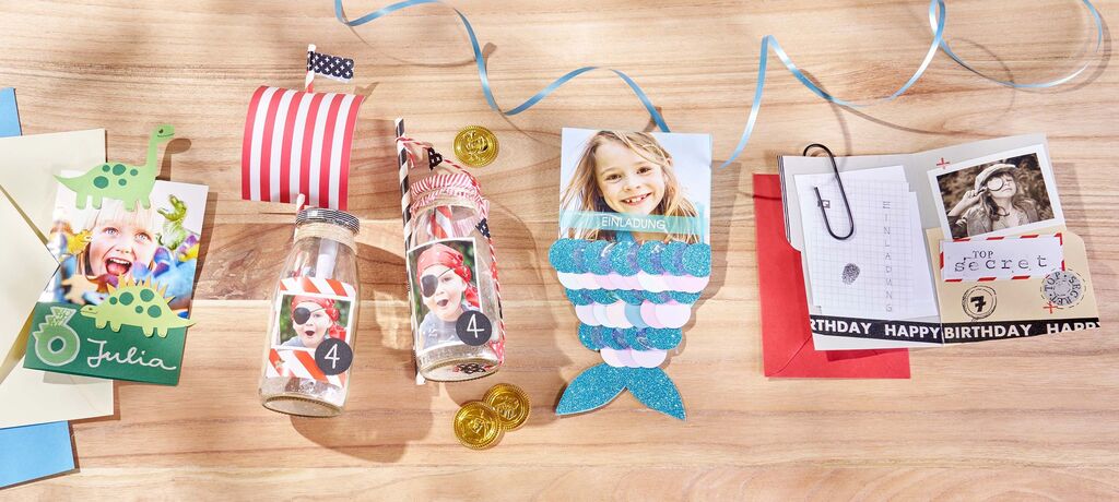 Bunte Grußkarten in verschiedenen Designs auf einem Tisch, darunter ein Schiffsmodell, Flaschen mit Etiketten und eine Meerjungfrau-Karte