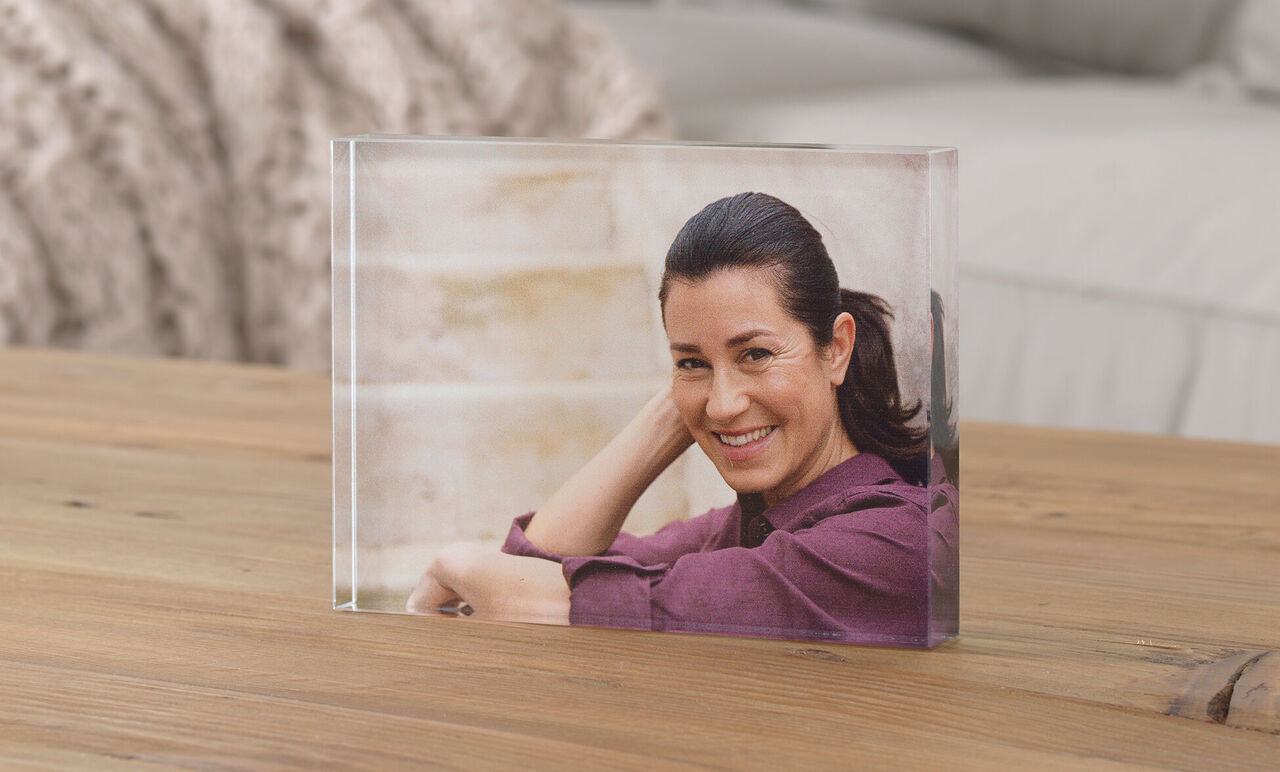 Transparentes Foto in einem Block auf einem Holztisch, Person sitzt entspannt und lächelt.