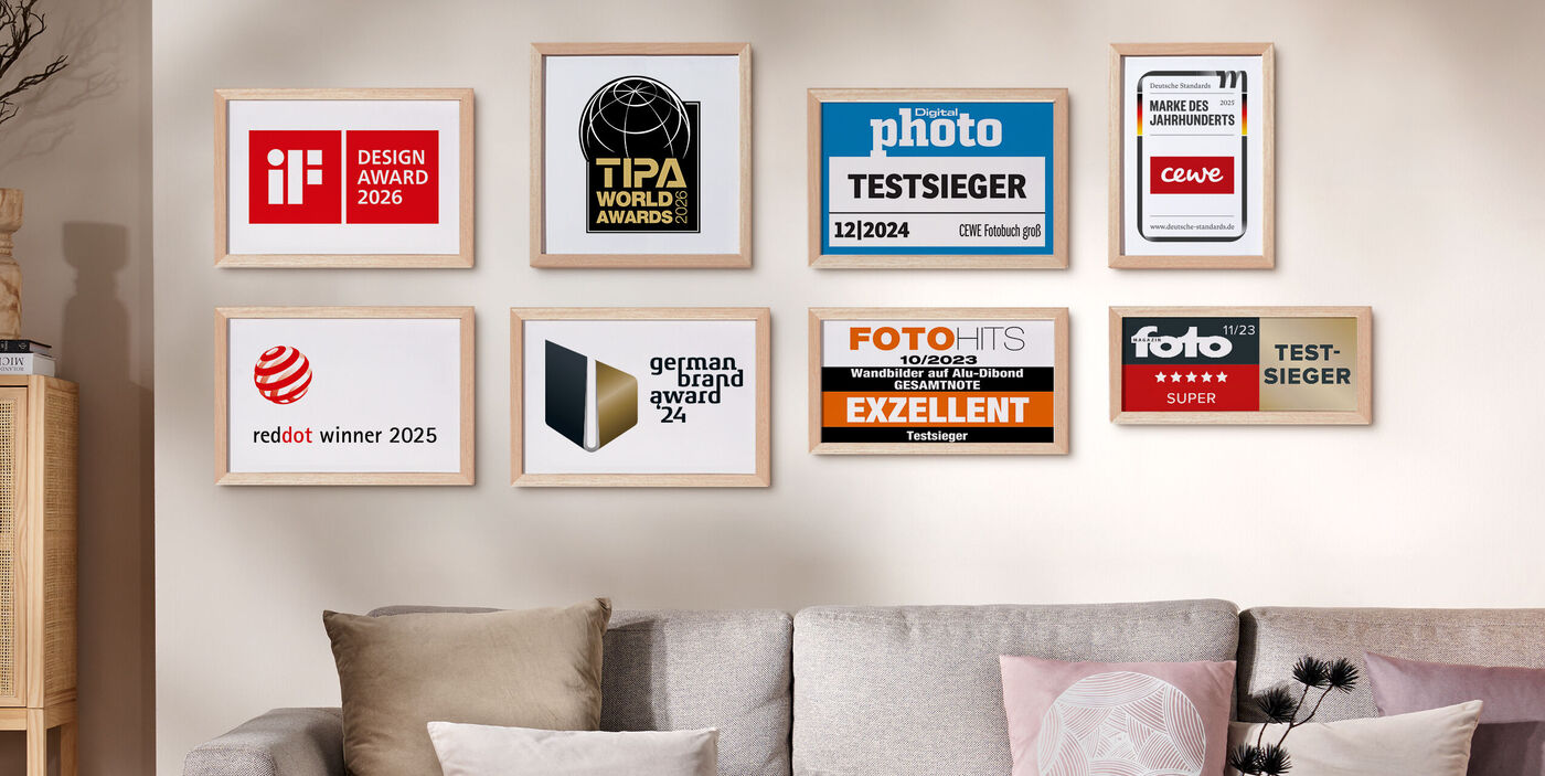 Mehrere gerahmte Auszeichnungen und Testsiegel von CEWE hängen an einer Wand über einem Sofa und stehen für geprüfte Qualität und Vertrauen