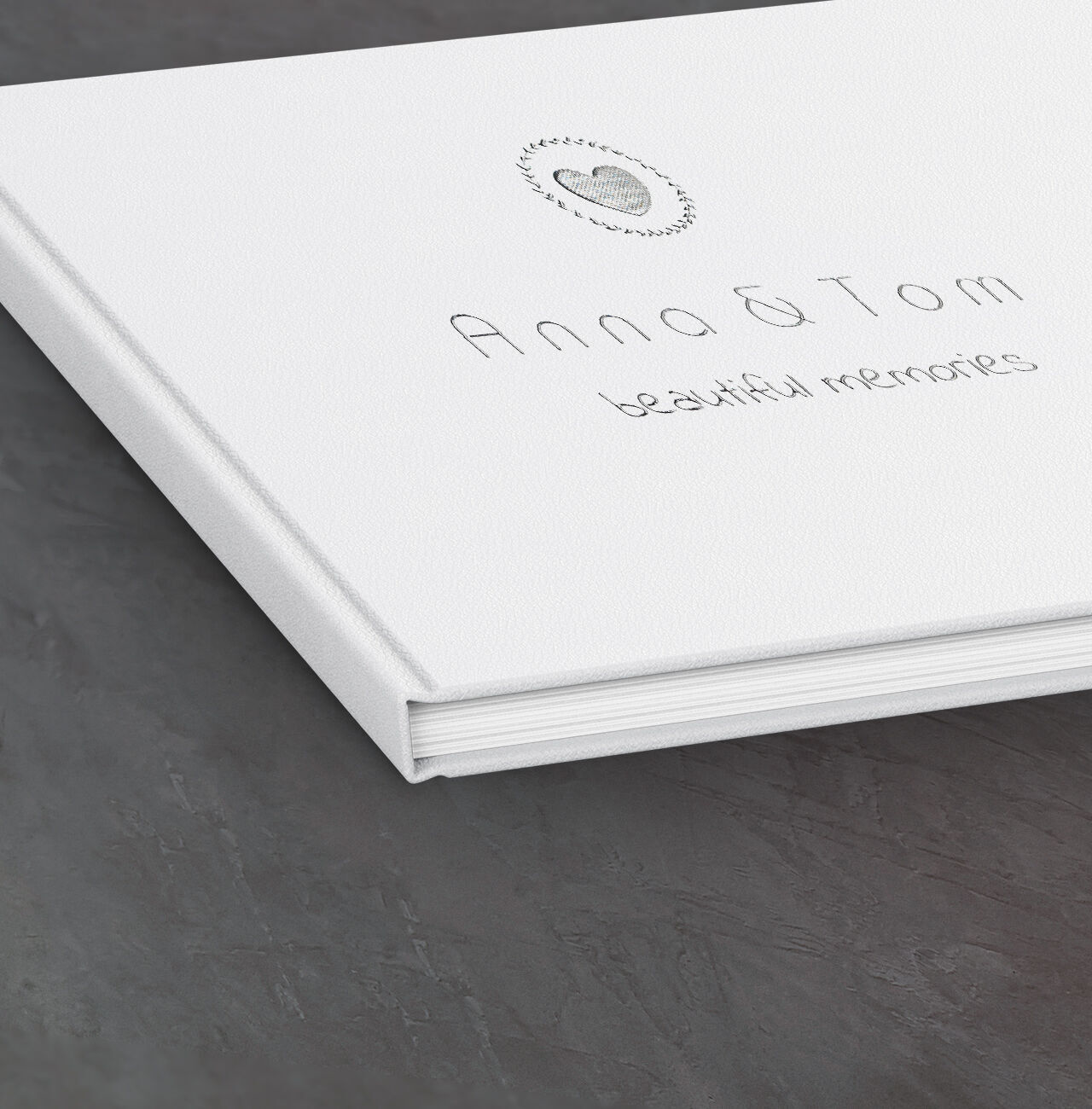 Weißes Fotobuch mit dem Titel 'Anna & Tom - beautiful memories' auf einem dunklen Tisch.