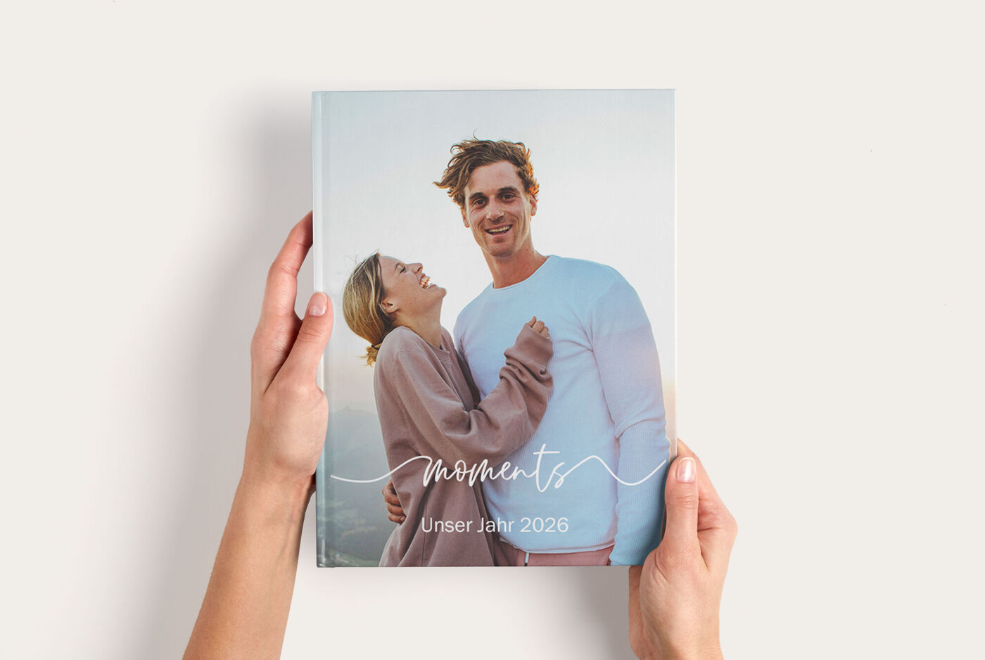 Das CEWE Fotobuch mit dem Titel 'moments' wird von zwei Personen gehalten. Es zeigt ein schönes Cover mit einem emotionalen Moment.