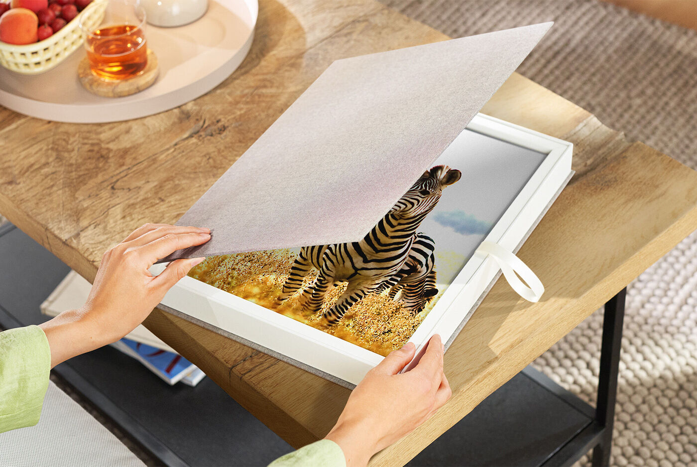 Person öffnet eine Geschenkbox, in der ein gerahmtes Foto eines Zebras in einer Savannenlandschaft liegt.