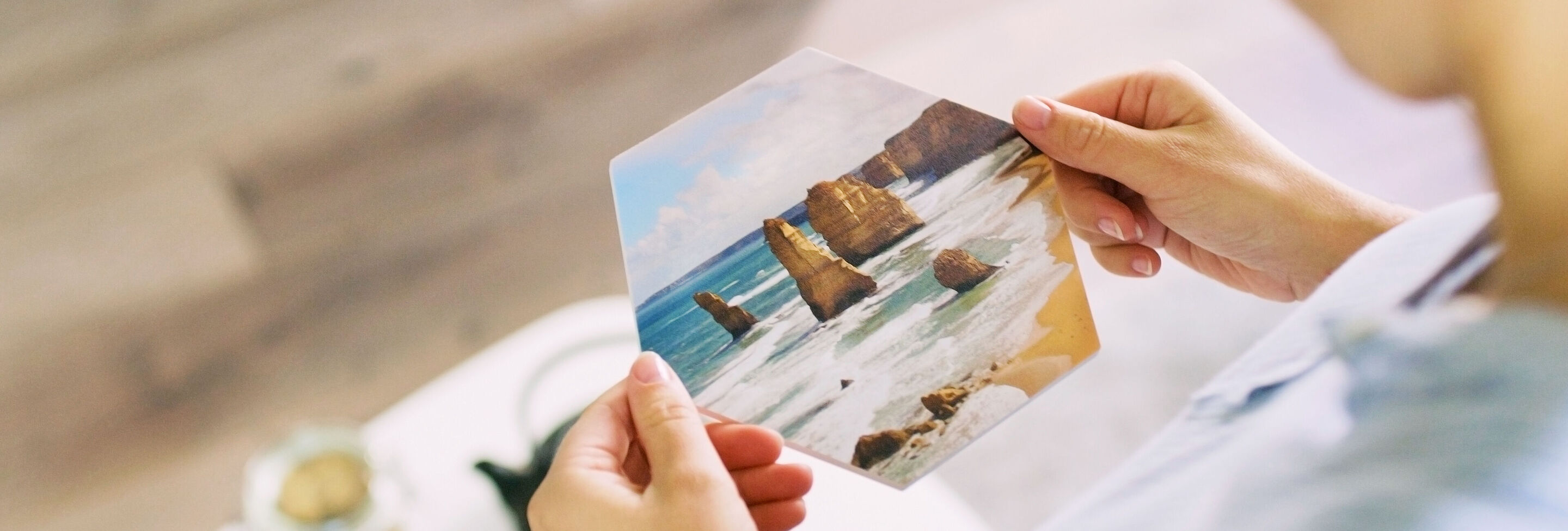 Eine Person hält ein Bild mit Strandmotiven und Felsen in den Händen