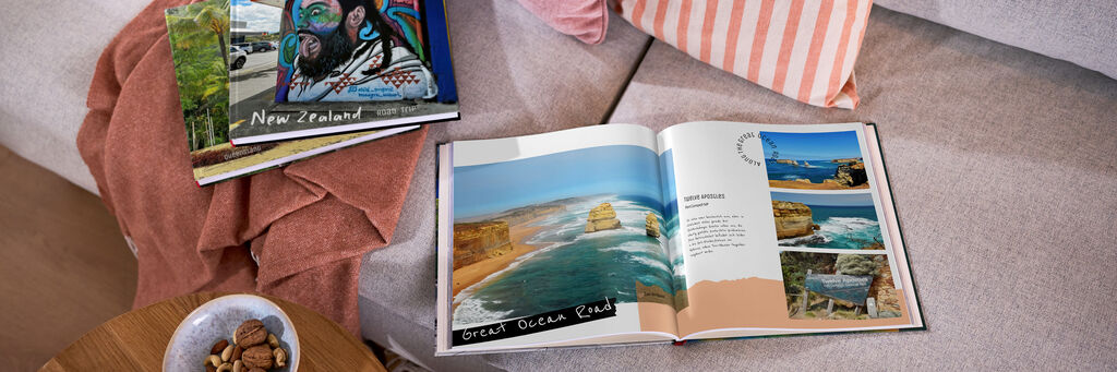 Offenes CEWE FOTOBUCH mit Fotos einer Australienreise auf einem Sofa. Zwei weitere Exemplare liegen daneben.