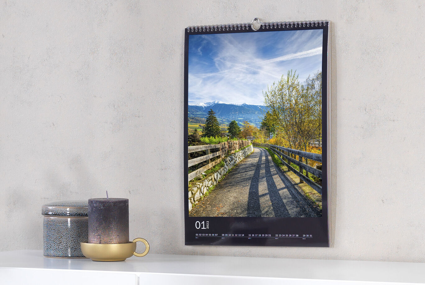 Ein schöner Wandkalender mit einem Landschaftsmotiv. Der Kalender zeigt einen Sonnenaufgang über einem Waldweg, umgeben von Bäumen und Bergen.