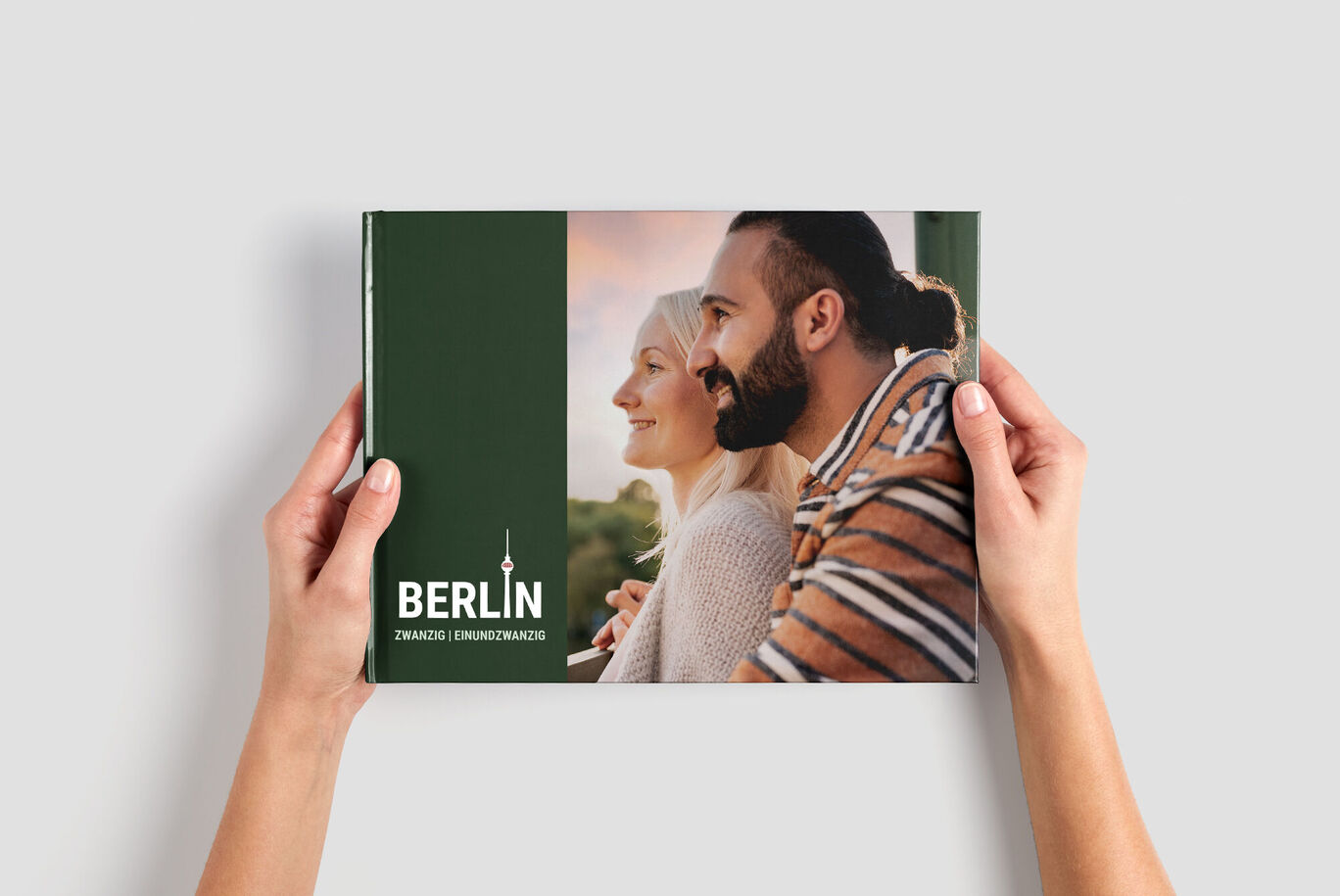 Eine Person hält ein CEWE FOTOBUCH mit einem Cover in grün und der Aufschrift 'Berlin'