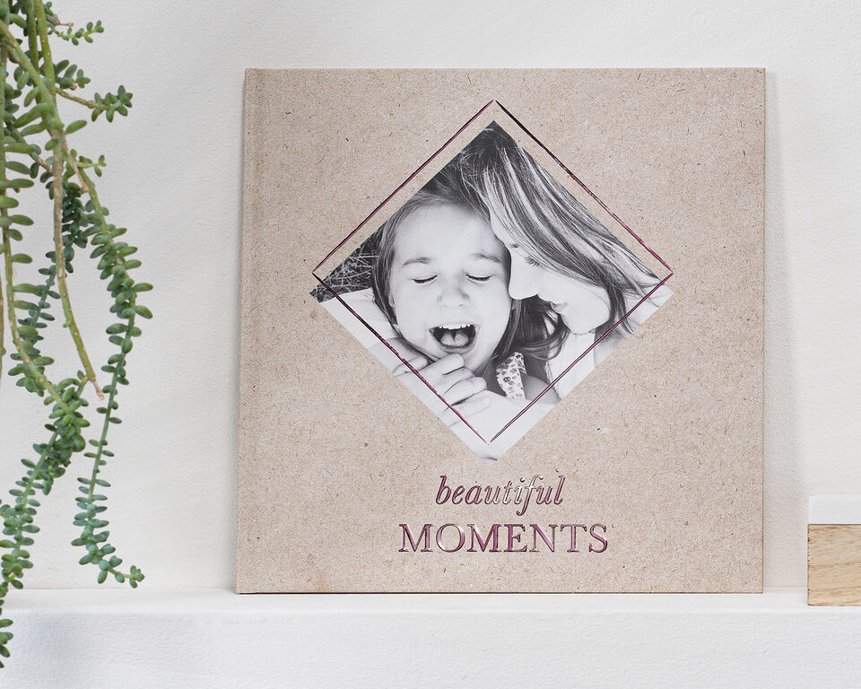 Ein handgefertigtes CEWE Fotobuch mit dem Titel 'beautiful Moments' auf einem Tisch, umgeben von Pflanzen.