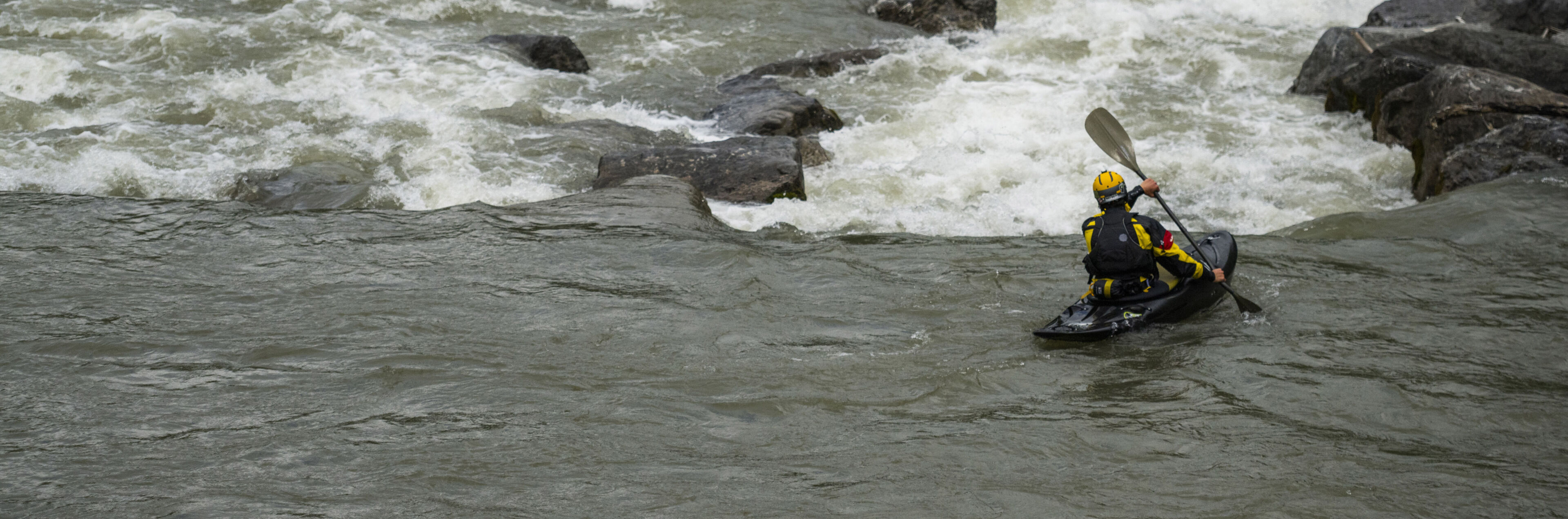 Eine Person fährt in einem Kajak auf einem Fluss. Direkt vor ihr liegt eine enge Flussstelle.
