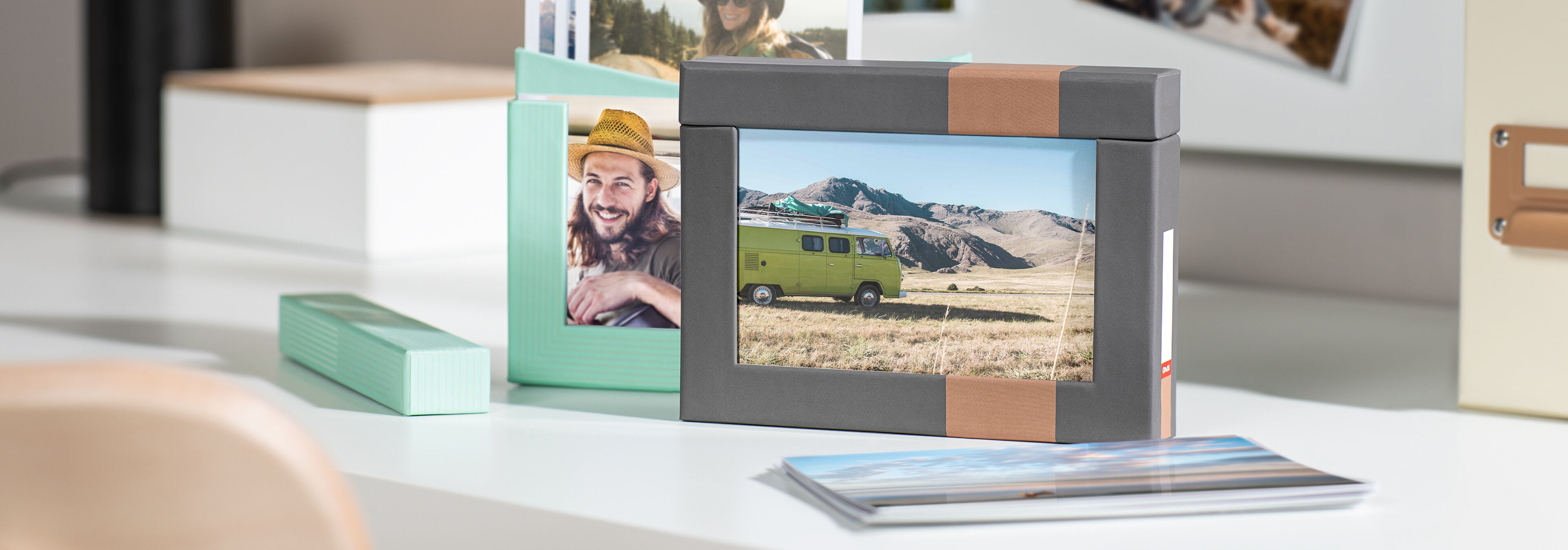 Eine kreative Anordnung von Foto-Boxen und Bildern auf einem Tisch, inklusive einer Foto-Box in Grau und einer in Mint, mit einem Foto eines Campingbusses.