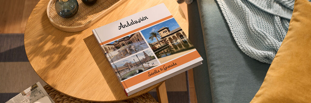 Auf einem kleinen Holztisch liegt ein CEWE FOTOBUCH. Darauf sind drei Fotos und der Schriftzug "Andalusien" zu sehen.