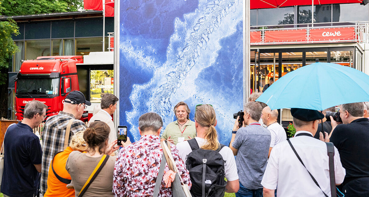 Mehrere Menschen sind vor einer großen Fotoleinwand versammelt. Im Hintergrund steht der CEWE Truck.