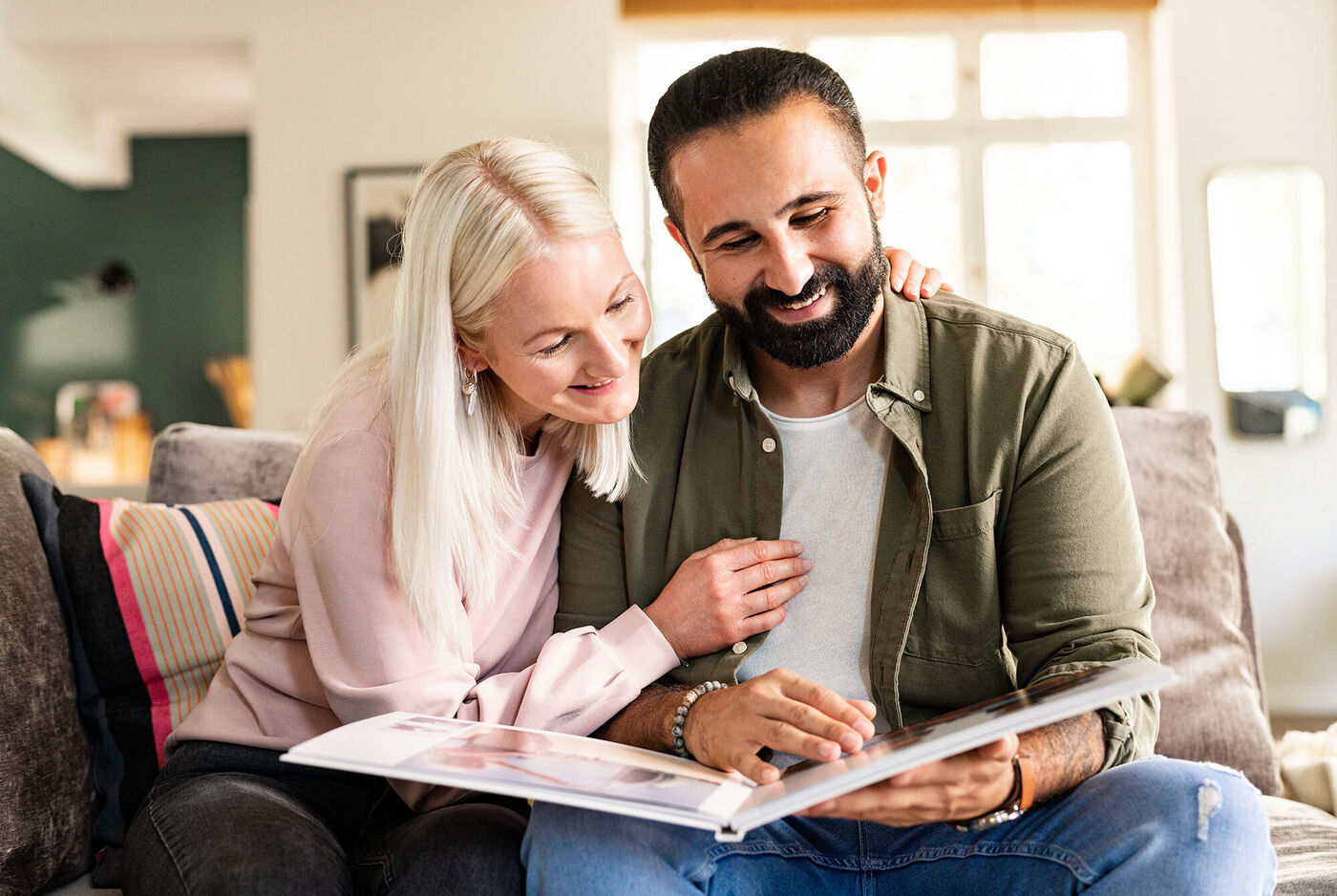 Ein Paar blättert gemeinsam in einem Fotobuch auf einer Couch und genießt gemeinsame Erinnerungen