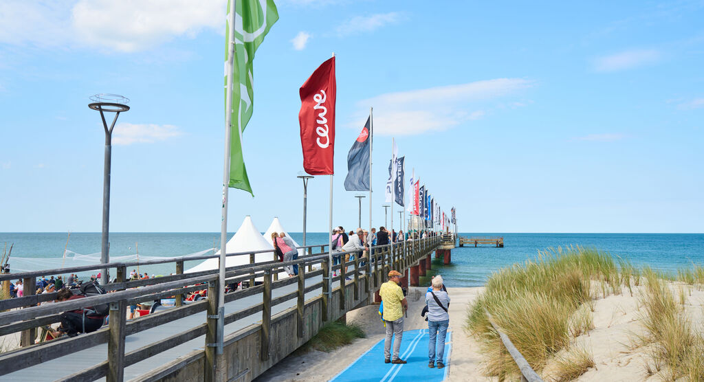Auf einem Steg an einem Strand wehen mehrere bunten Fahnen, darunter eine Fahne mit CEWE Logo.