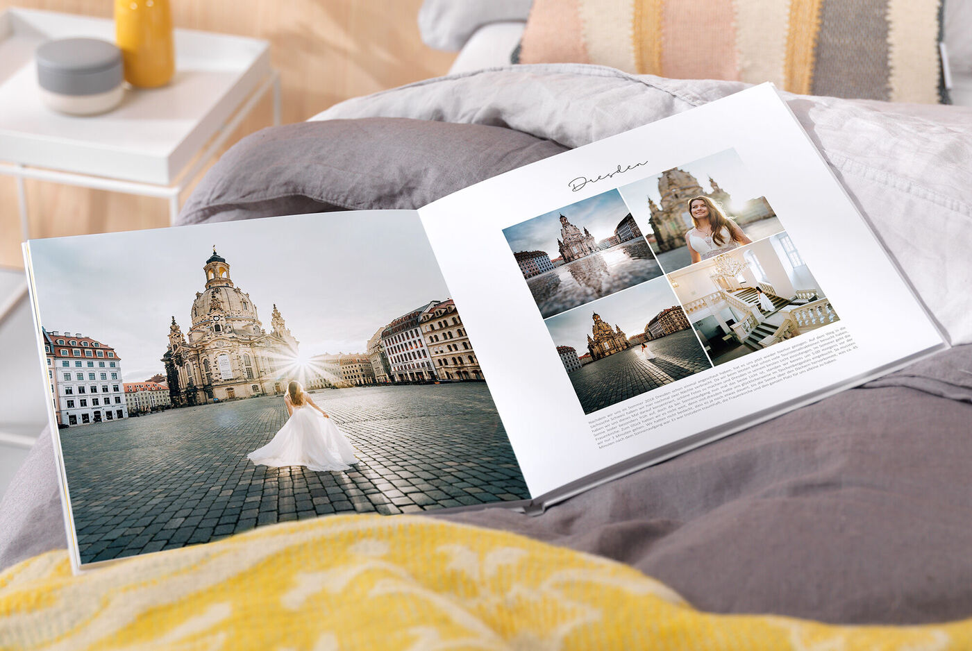 Ein geöffnetes CEWE Fotobuch liegt auf einem gemütlichen Bett. Auf der linken Seite sieht man eine Frau in einem weißen Kleid vor der Frauenkirche in Dresden. Auf der rechten Seite sind verschiedene Fotos der Stadt zu sehen.