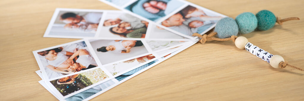 Bunte Fotokarten mit Familienmotiven liegen auf einem Tisch, dazu eine Holzkette mit dem Namen 'Niklas'.
