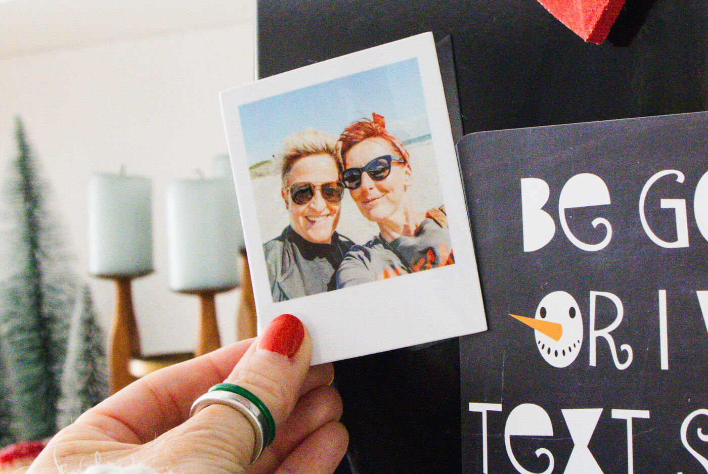 Eine Hand hält ein Polaroidfoto von zwei Personen, die zusammen am Strand sind.