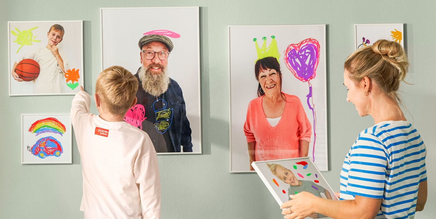 Kind und Erwachsene gestalten bunte CEWE Poster mit Zeichnungen und Farben in einem hellen Raum