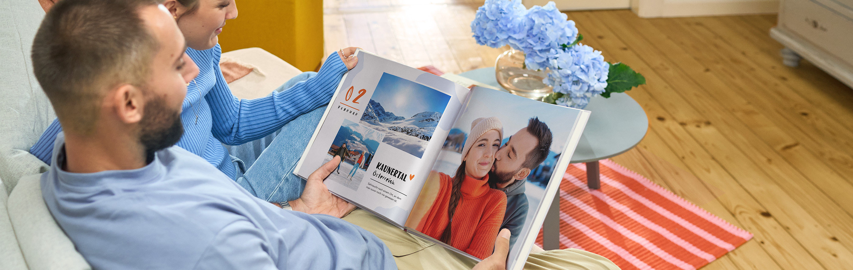 Zwei Personen sitzen auf Sofa und schauen gemeinsam in ein CEWE FOTOBUCH mit Schneebildern