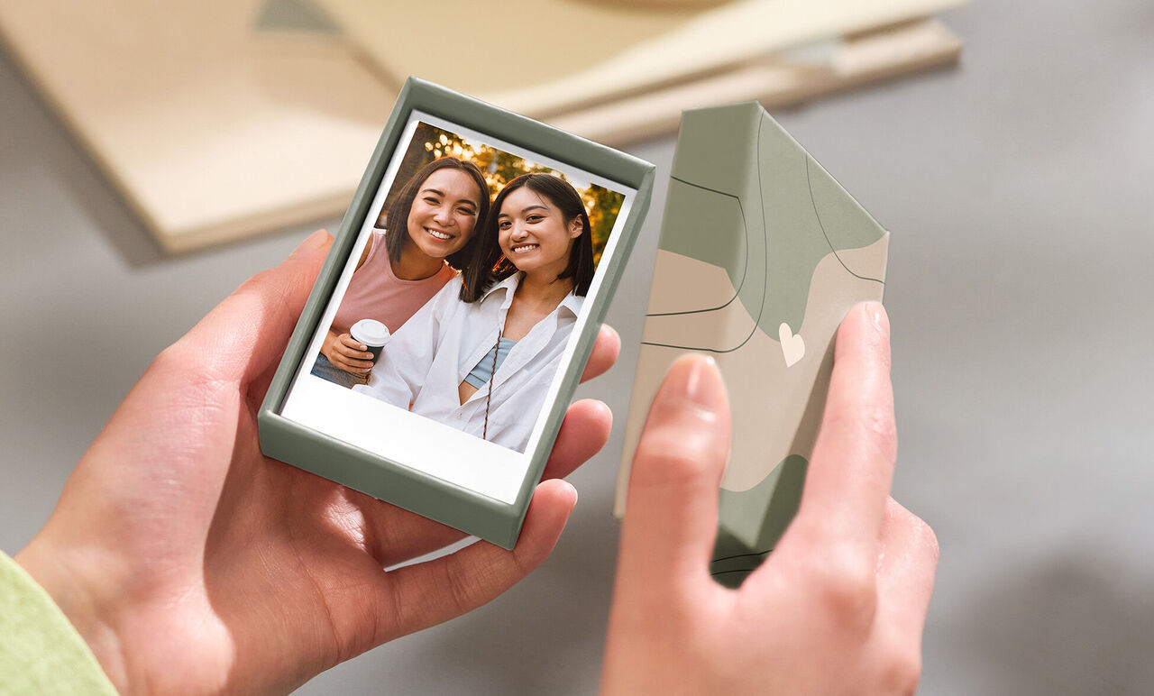Eine Person hält eine kleine Geschenkbox mit einem Foto von Freunden, die eine glückliche Zeit zusammen verbringen. Die Box sieht ansprechend aus.