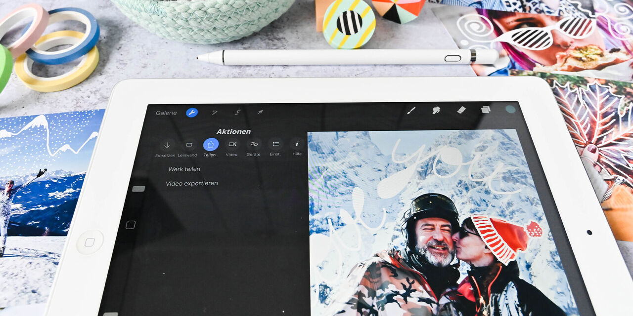 Zwei Personen in warmer Kleidung bei Schnee, auf einem Tablet wird ein kreatives Design bearbeitet.