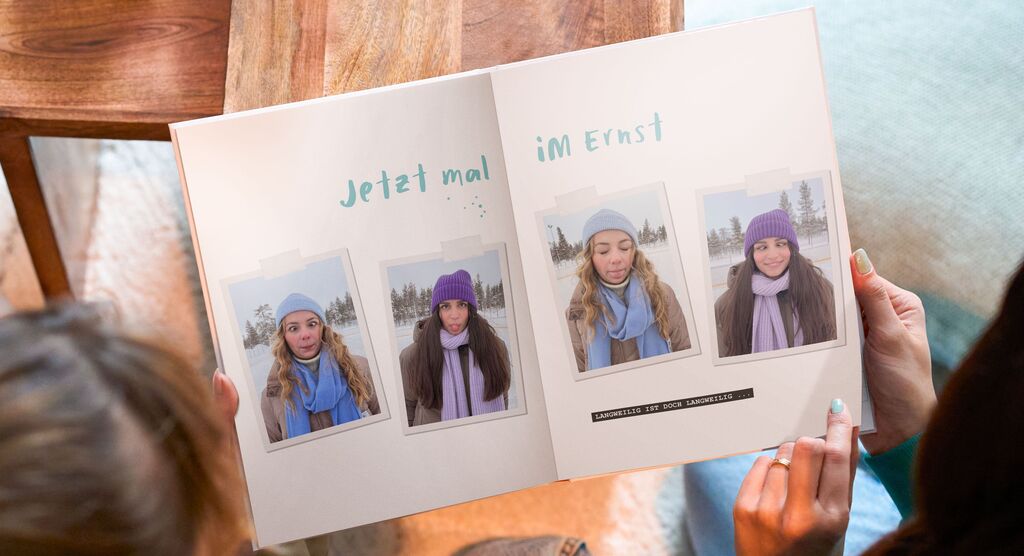 Eine Person zeigt stolz ein geöffnetes Fotobuch mit Freunden im Schnee.