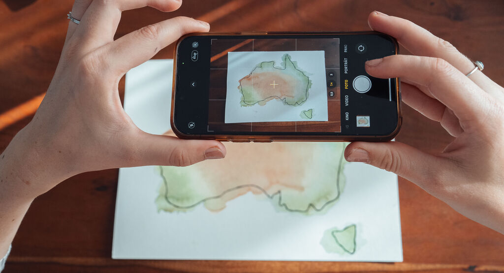 Eine Person hält ein Handy, um eine Aquarellkarte von Australien zu fotografieren.