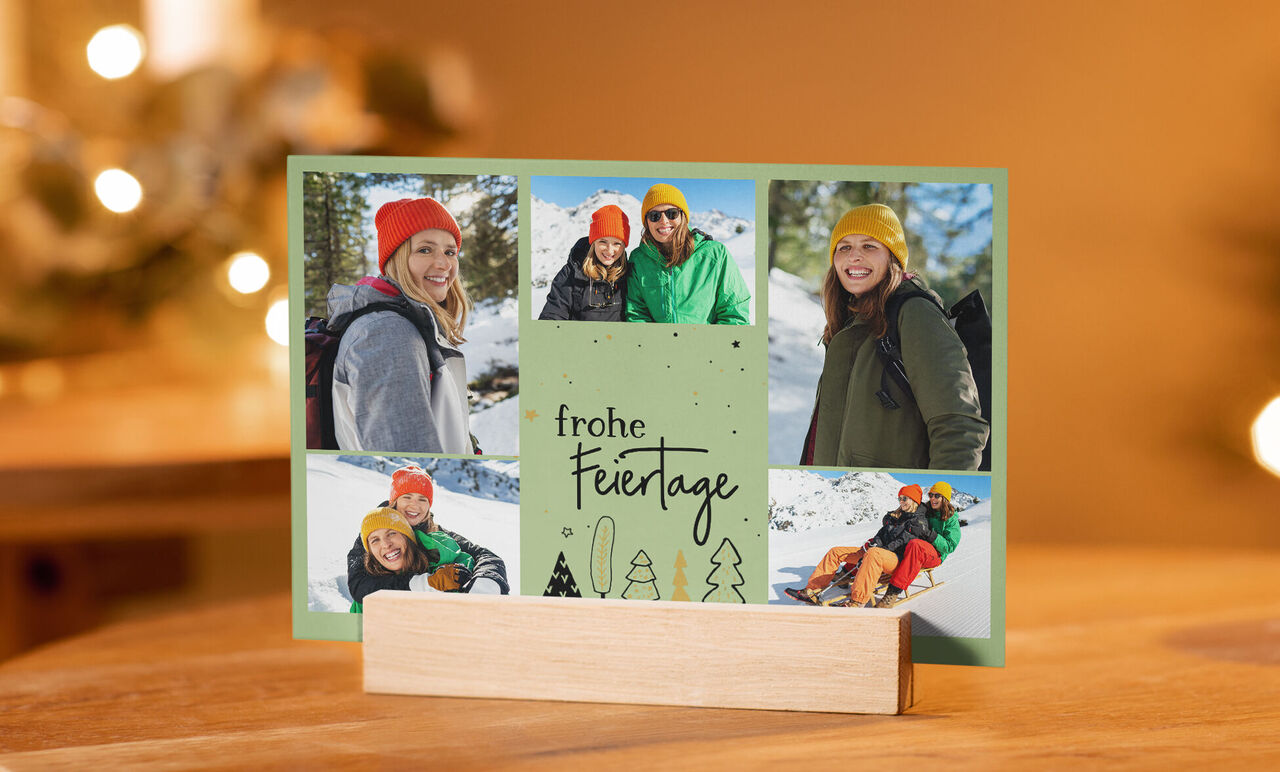Eine festliche Grußkarte mit multikulturellen Menschen in warmen Pullovern und farbenfrohen Mützen, die fröhlich im Schnee sitzen und naturverbundene Momente teilen. Der Text "frohe Feiertage" ziert die Karte.