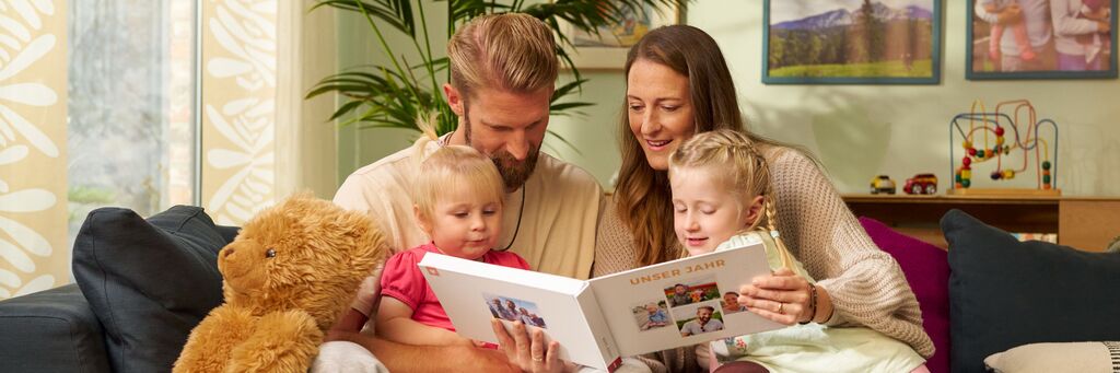 Ein junge Familie sitzt auf einem Sofa und schaut gemeinsam ein CEWE FOTOBUCH an.