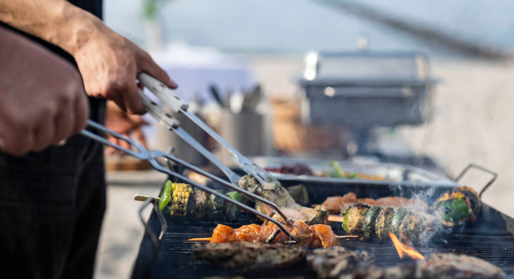 Dieses Motiv zeigt eine Nahaufnahme eines Grills. Auf dem Rost liegen Grill-Fleisch und  Gemüsespieße