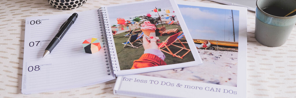 Ein offener Fotokalender mit bunten Urlaubsfotos und einem Notizbuch auf einem Tisch